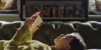 Od pierwszego Harlequina do domowej biblioteki: historia pewnej czytelniczki Młoda kobieta leży na sofie i czyta książkę w domowym zaciszu